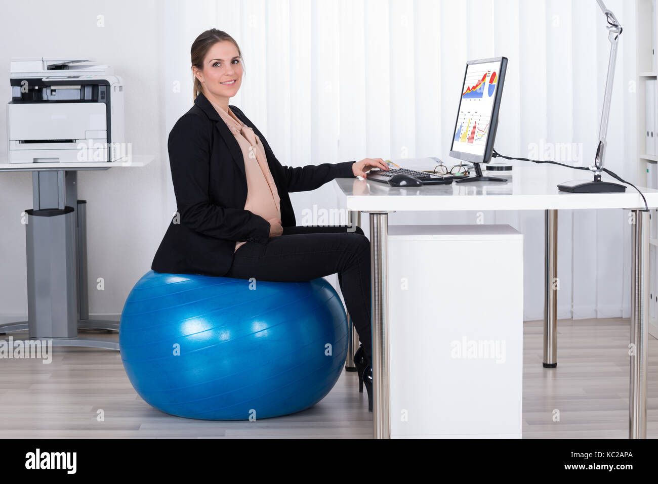 Femmes enceintes businesswoman sitting on fitness ball tout en travaillant sur computer in office Banque D'Images