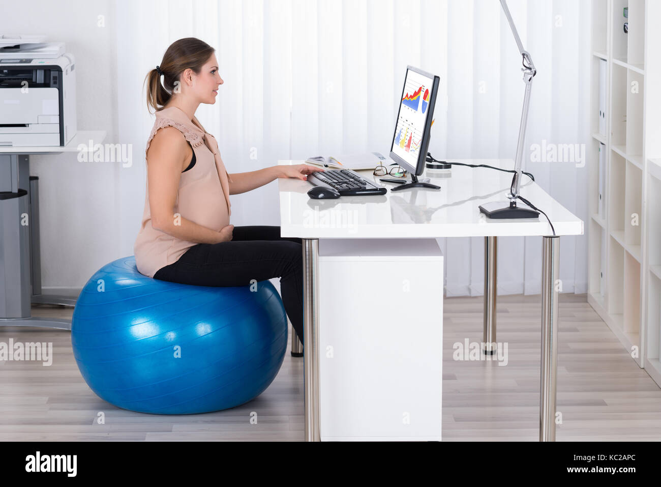 Young pregnant woman sitting on fitness ball tout en regardant le graphique in office Banque D'Images