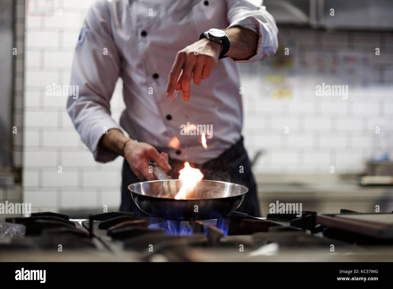 Un homme cuit la cuisson friteuses dans un feu de cuisine. Banque D'Images