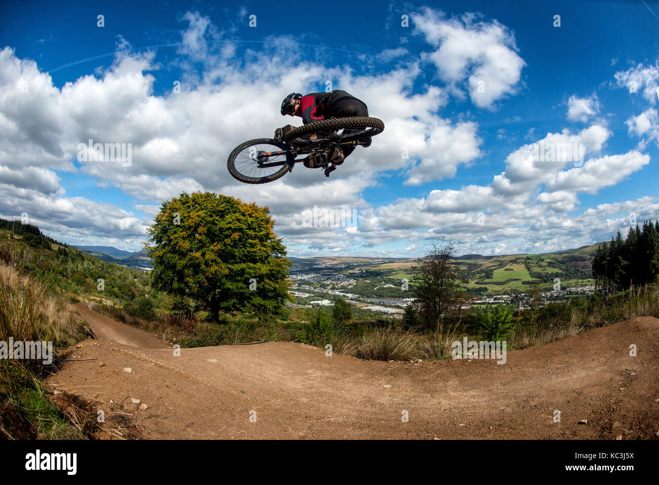 Un vélo de montagne équitation saute pendant un sentier au Bikepark de galles surplombant la ville de Merthyr Tydfil et les Brecon Beacons sur l'horizon. Banque D'Images