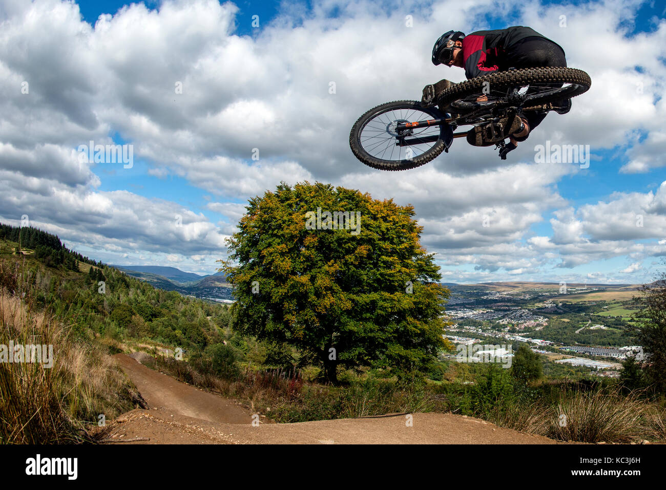 Un vélo de montagne équitation saute pendant un sentier au Bikepark de galles surplombant la ville de Merthyr Tydfil et les Brecon Beacons sur l'horizon. Banque D'Images