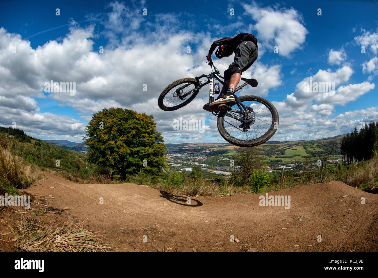 Un vélo de montagne équitation saute pendant un sentier au Bikepark de galles surplombant la ville de Merthyr Tydfil et les Brecon Beacons sur l'horizon. Banque D'Images