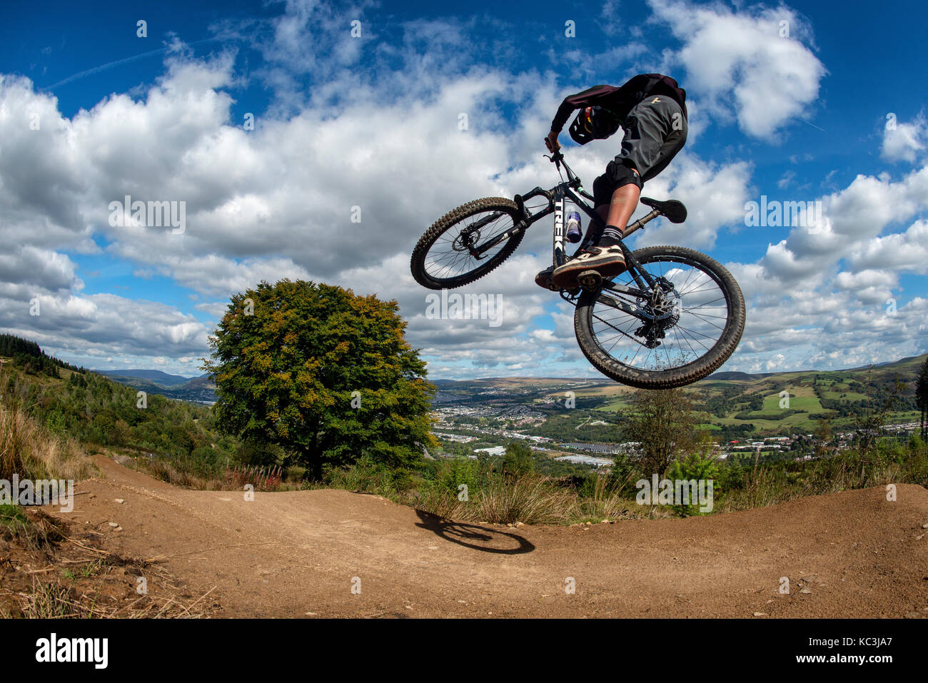 Un vélo de montagne équitation saute pendant un sentier au Bikepark de galles surplombant la ville de Merthyr Tydfil et les Brecon Beacons sur l'horizon. Banque D'Images