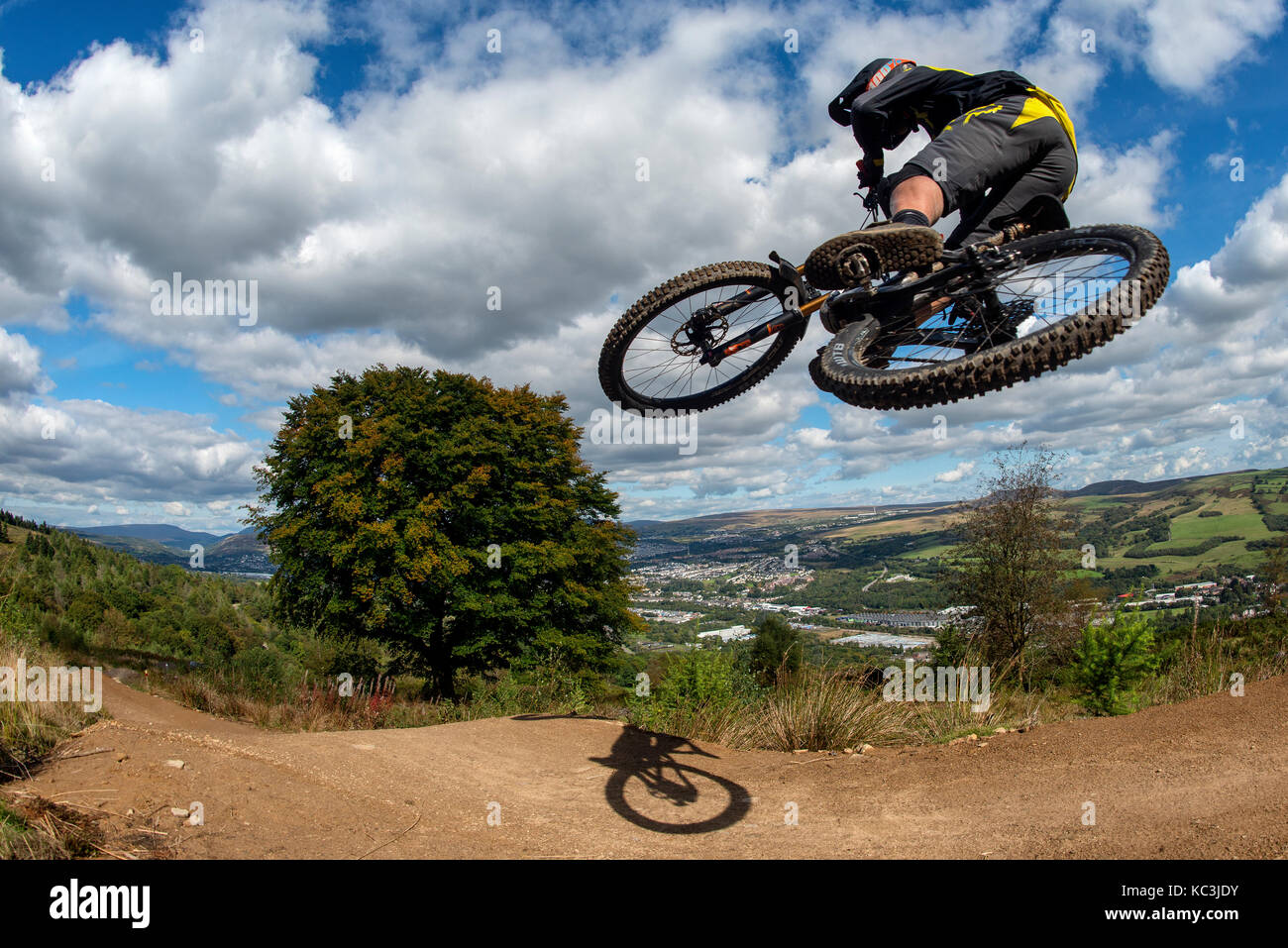 Un vélo de montagne équitation saute pendant un sentier au Bikepark de galles surplombant la ville de Merthyr Tydfil et les Brecon Beacons sur l'horizon. Banque D'Images