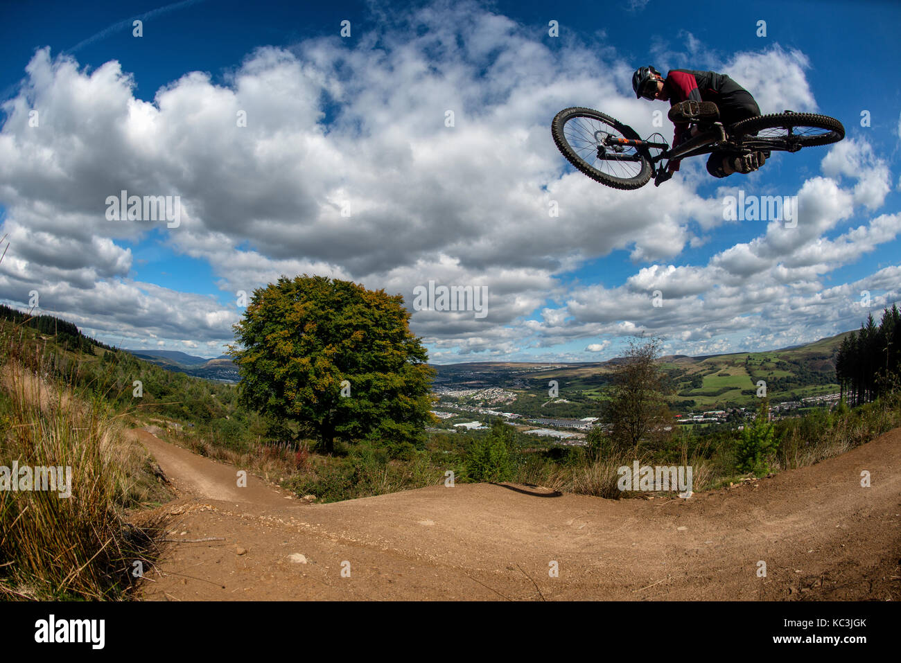Un vélo de montagne équitation saute pendant un sentier au Bikepark de galles surplombant la ville de Merthyr Tydfil et les Brecon Beacons sur l'horizon. Banque D'Images