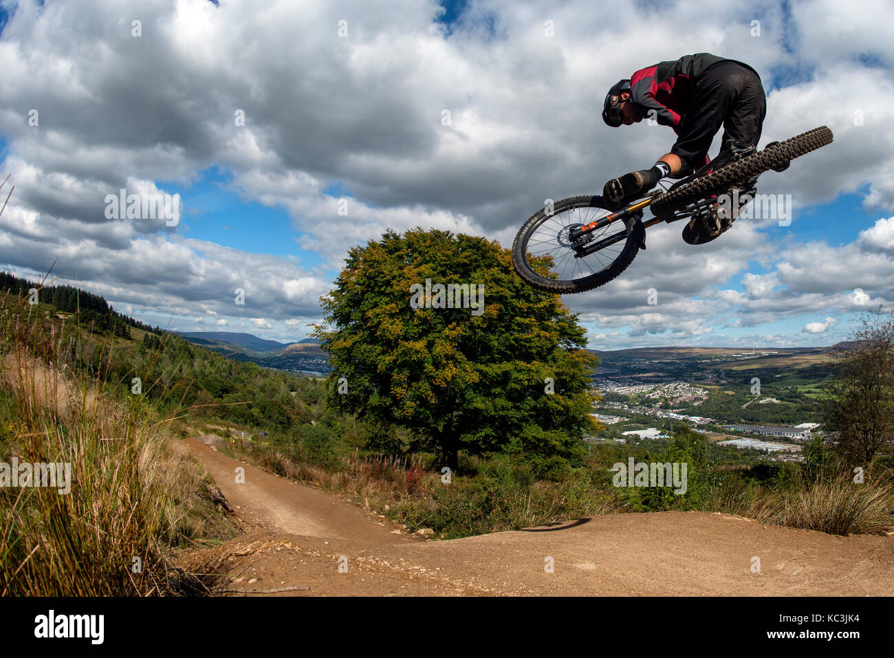 Un vélo de montagne équitation saute pendant un sentier au Bikepark de galles surplombant la ville de Merthyr Tydfil et les Brecon Beacons sur l'horizon. Banque D'Images