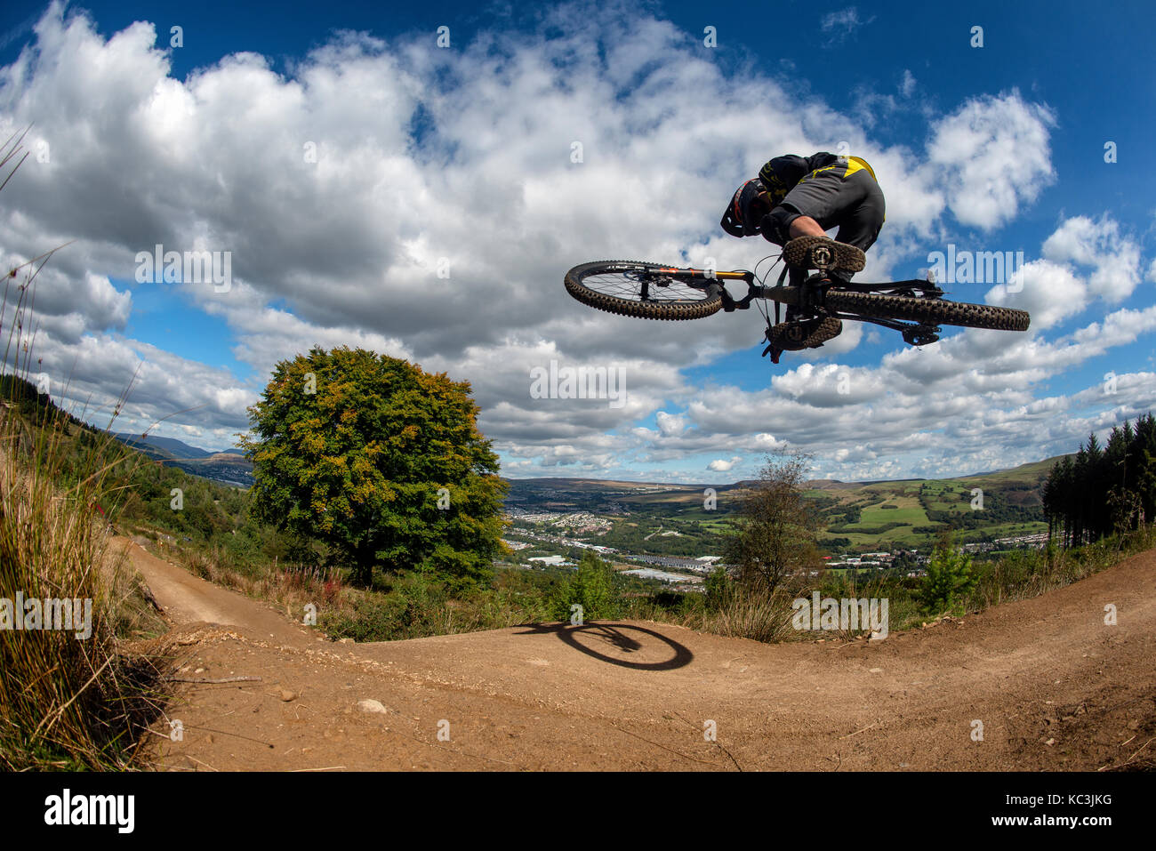 Un vélo de montagne équitation saute pendant un sentier au Bikepark de galles surplombant la ville de Merthyr Tydfil et les Brecon Beacons sur l'horizon. Banque D'Images