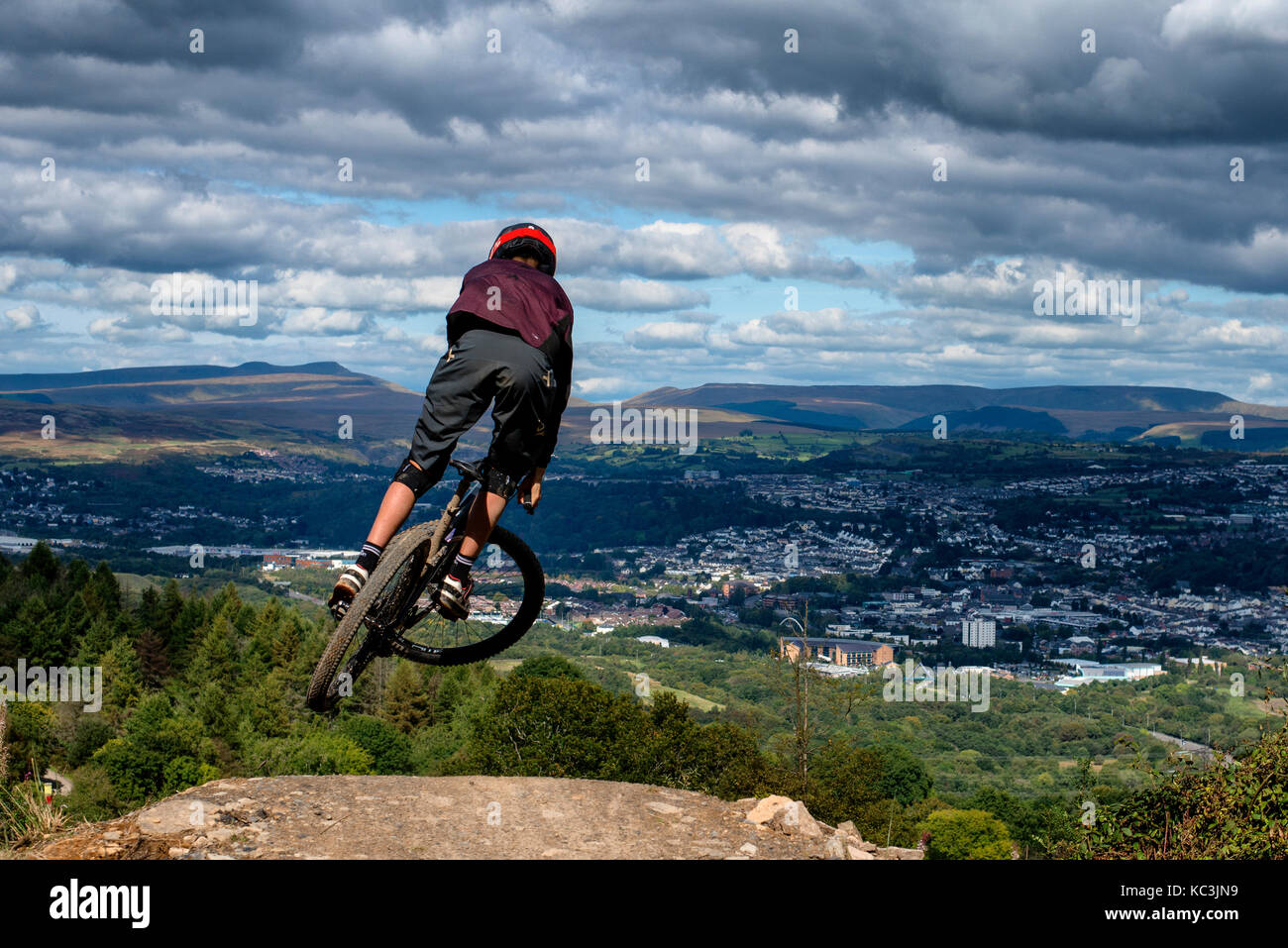 Un vélo de montagne équitation saute pendant un sentier au Bikepark de galles surplombant la ville de Merthyr Tydfil et les Brecon Beacons sur l'horizon. Banque D'Images
