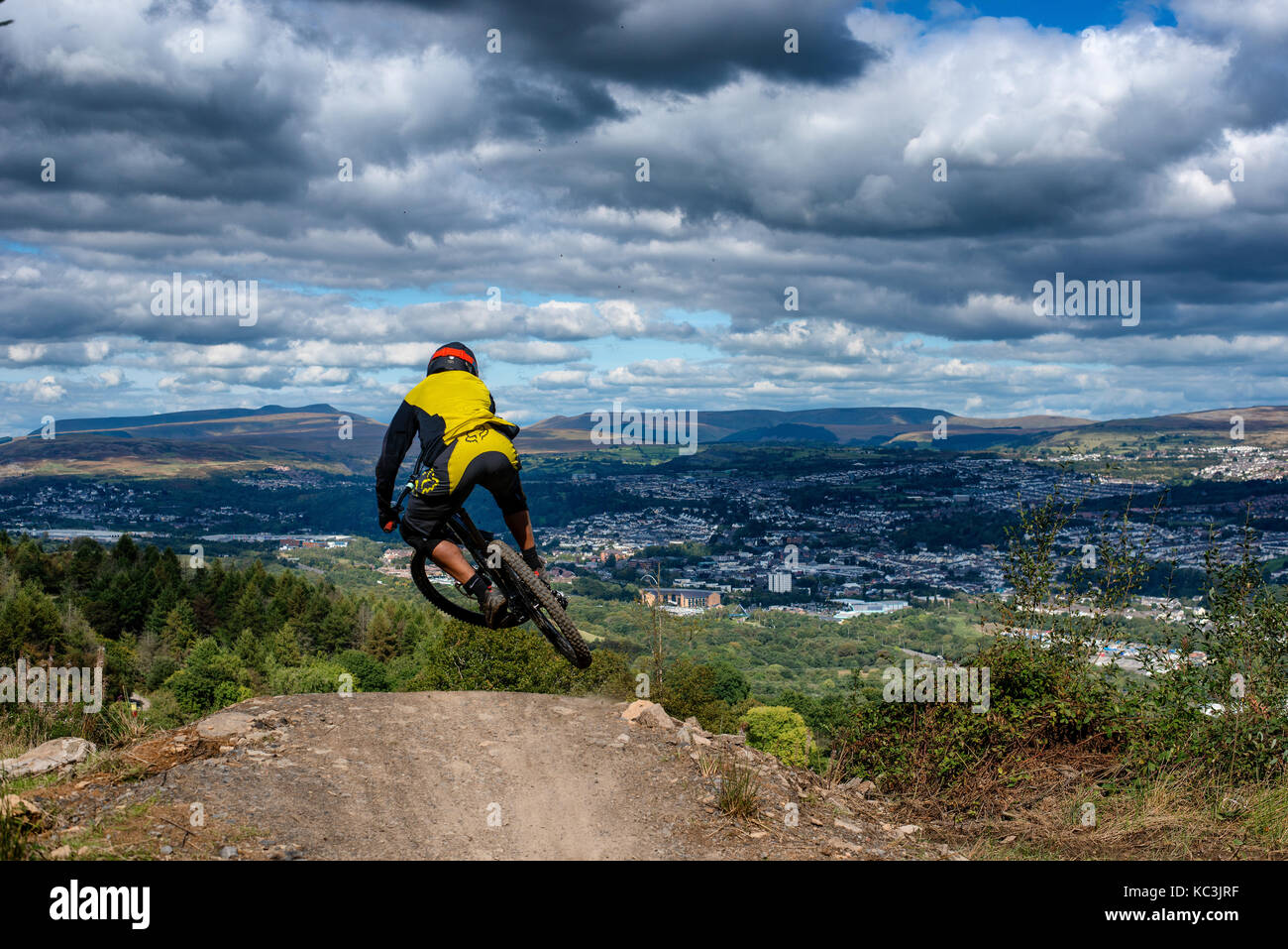 Un vélo de montagne équitation saute pendant un sentier au Bikepark de galles surplombant la ville de Merthyr Tydfil et les Brecon Beacons sur l'horizon. Banque D'Images