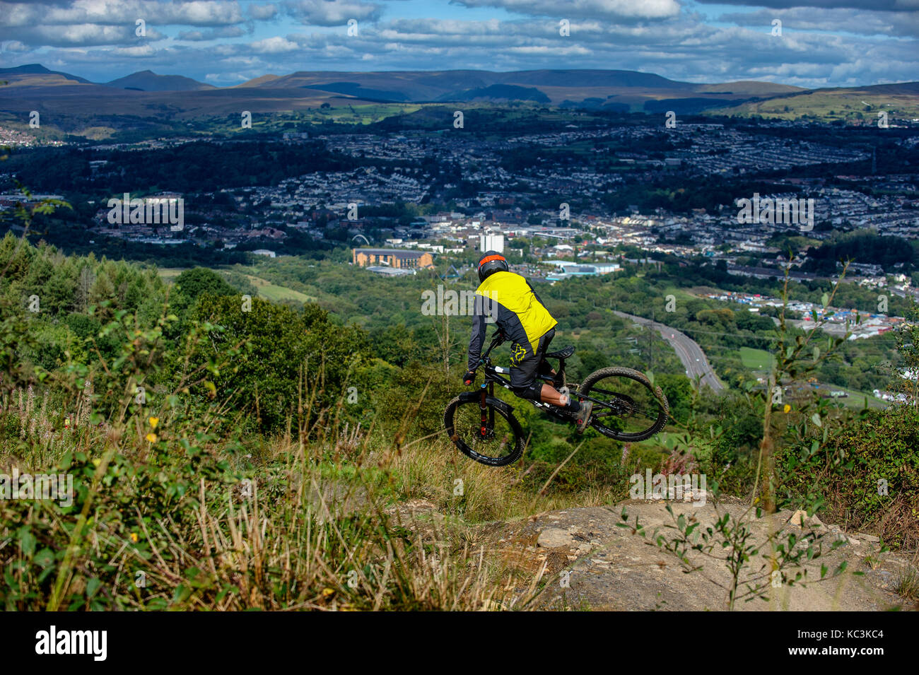 Un vélo de montagne équitation saute pendant un sentier au Bikepark de galles surplombant la ville de Merthyr Tydfil et les Brecon Beacons sur l'horizon. Banque D'Images