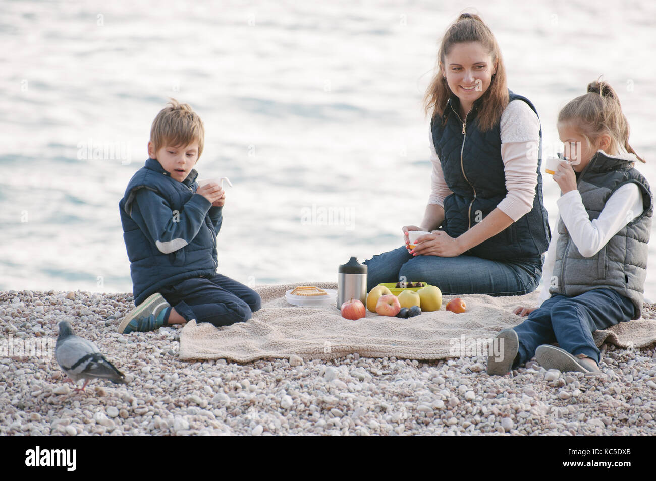 Mère heureuse avec deux enfants mignons on picnic à la mer par temps froid Banque D'Images