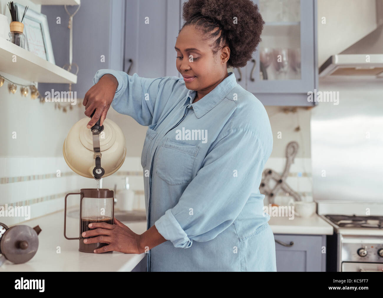 Souriante jeune femme africaine la préparation du café frais dans sa cuisine Banque D'Images