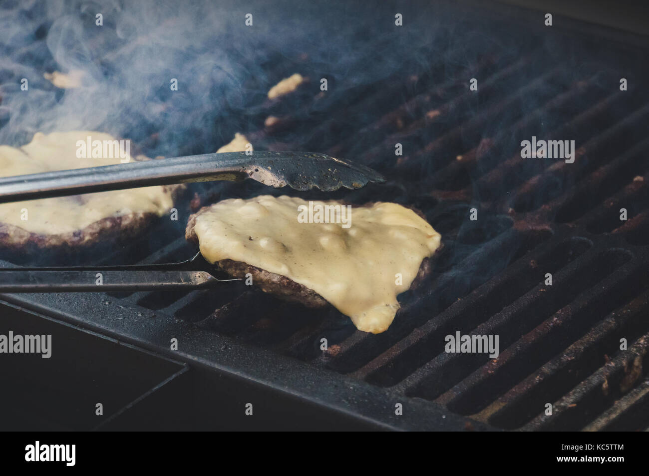 Burger de viande grillée avec du fromage sur le dessus et de légumes sur le grill en flammes. Faire fondre le fromage sur la galette sur le grill. chef flips hamburgers avec rencontré Banque D'Images