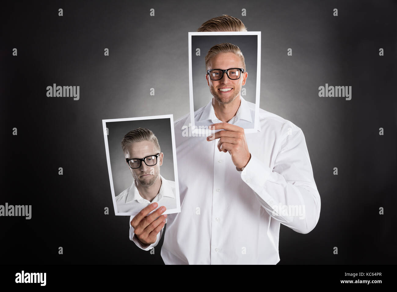 Sad man holding smiling photo en face de son visage sur fond noir Banque D'Images
