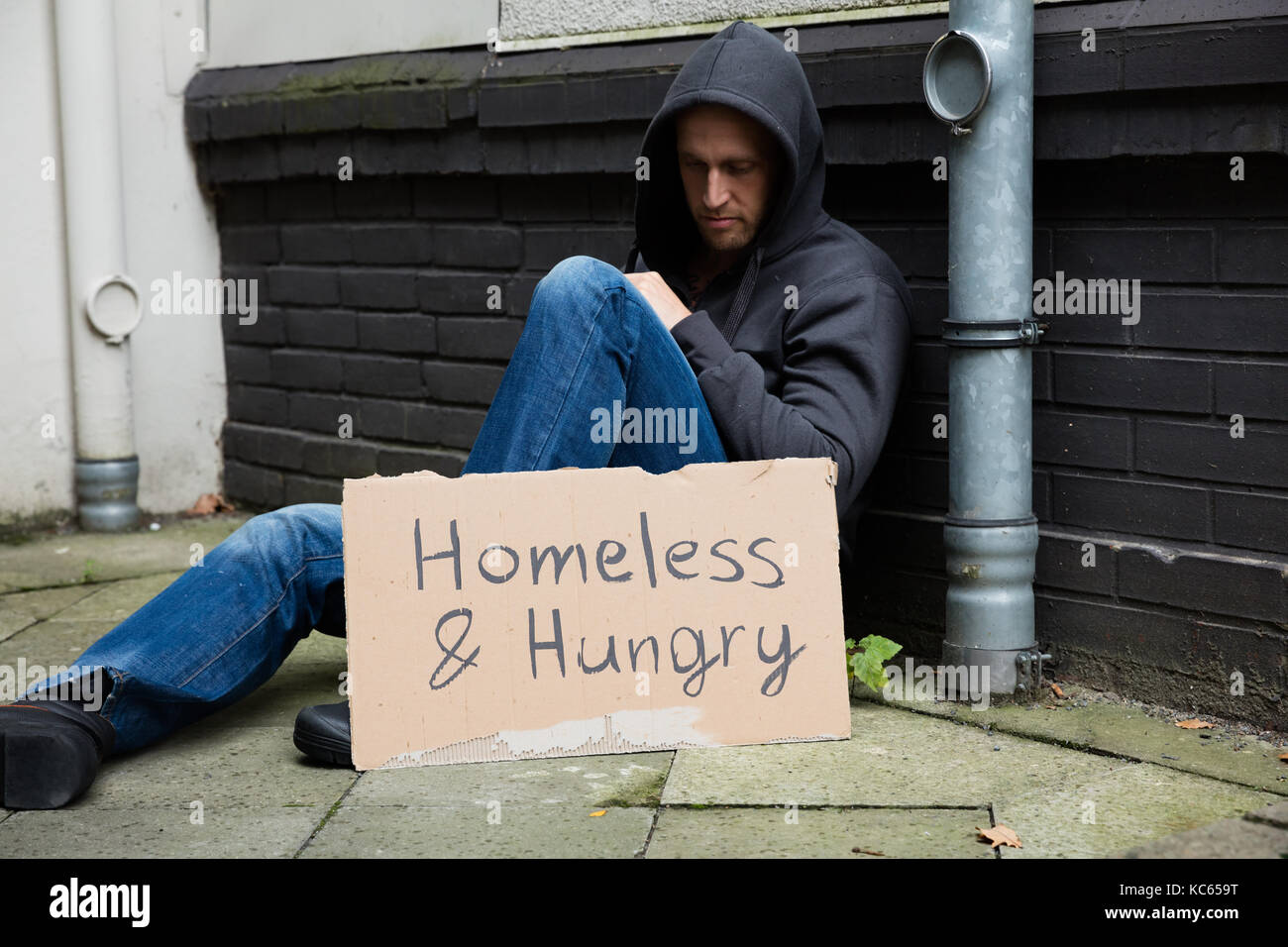 Les sans-abri et affamé homme assis sur rue avec pancarte Banque D'Images