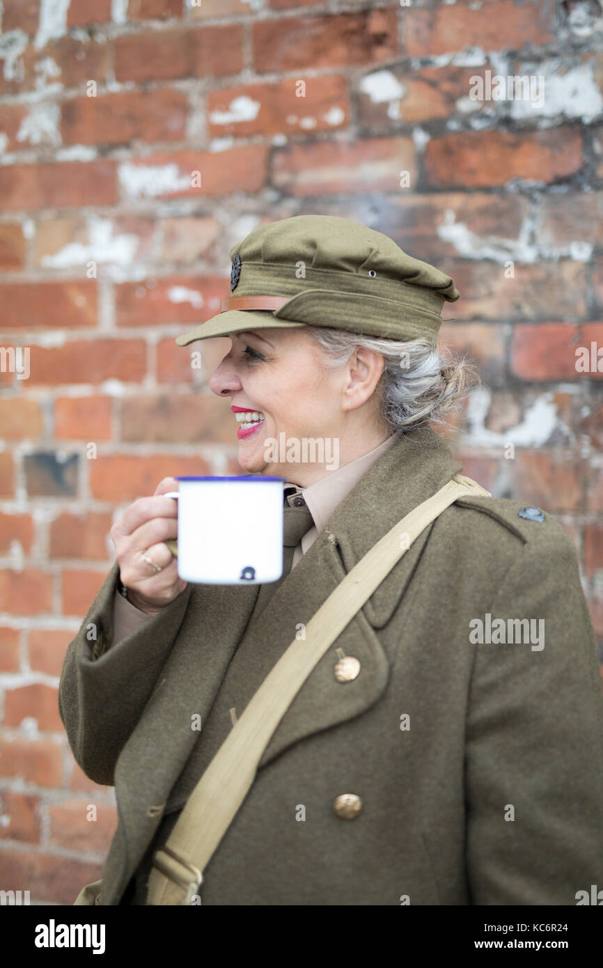 Dame habillée en uniforme vintage de l'armée britannique 1940' buvant du thé d'une tasse en étain. Welshpool UK 40's Weekend Banque D'Images