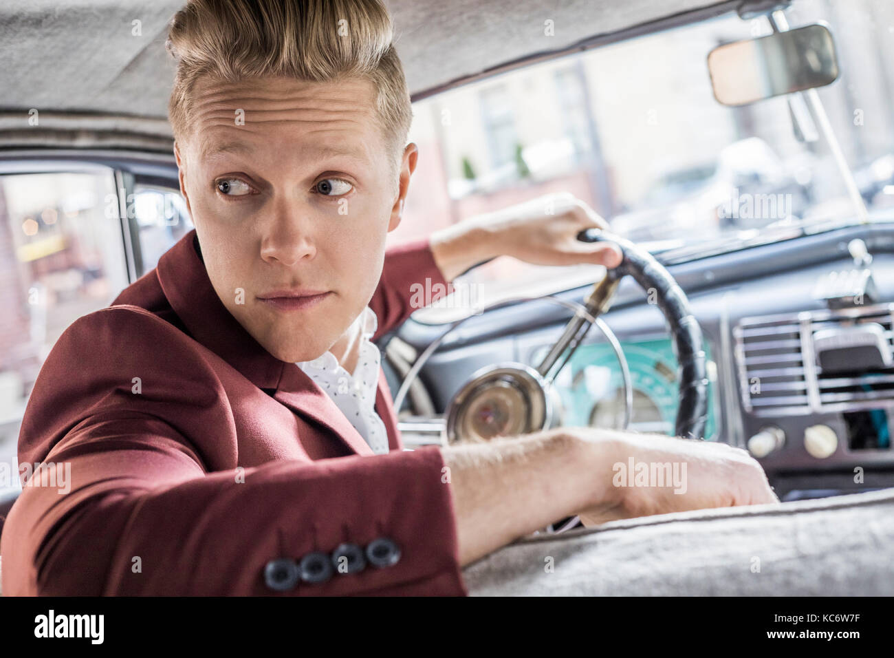 Homme conduisant vintage car, looking over shoulder Banque D'Images