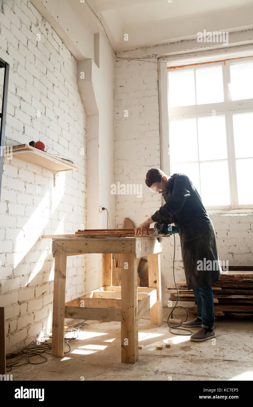 Professionnels qualifiés carpenter s'est concentré sur l'aide de l'outil de travail électrique en atelier de l'intérieur, couper du bois avec scie à main, artisan faisant custo Banque D'Images