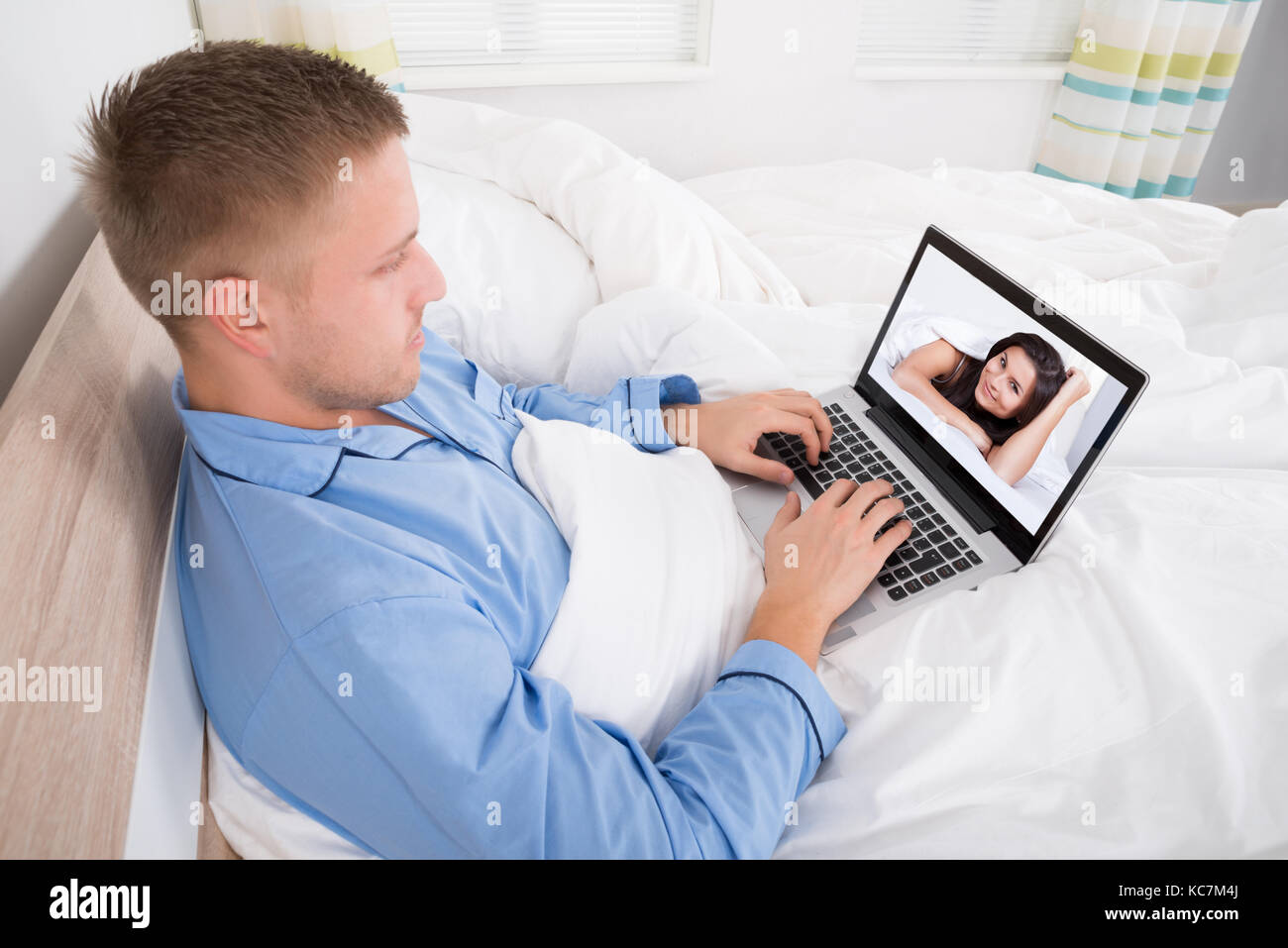 Jeune homme assis sur le lit le chat vidéo avec femme Banque D'Images