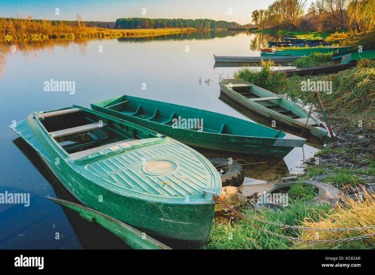 Fermer vue des chaloupes de pêche en bois vertes amarrées Skippets sur l'eau immobile sur la rive d'automne de la rivière. Banque D'Images