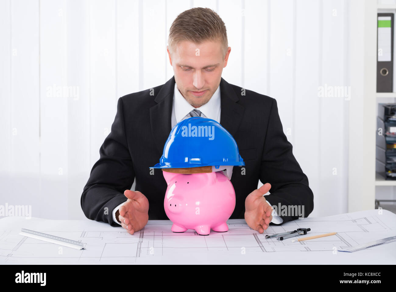 Architects piggybank portant un casque de construction sur blueprint at desk in office Banque D'Images