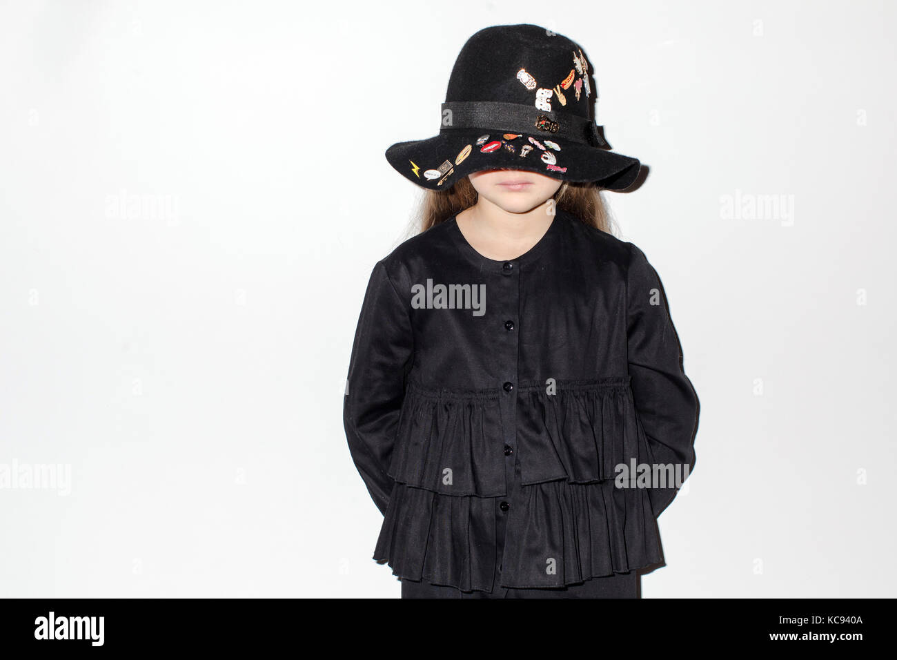 Sad little girl in black hat standing mur blanc Banque D'Images