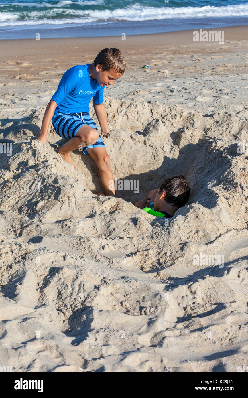 Avon, Outer Banks, Caroline du Nord, USA. Jeune garçon contrôle sur son frère, enterré dans le sable. Banque D'Images