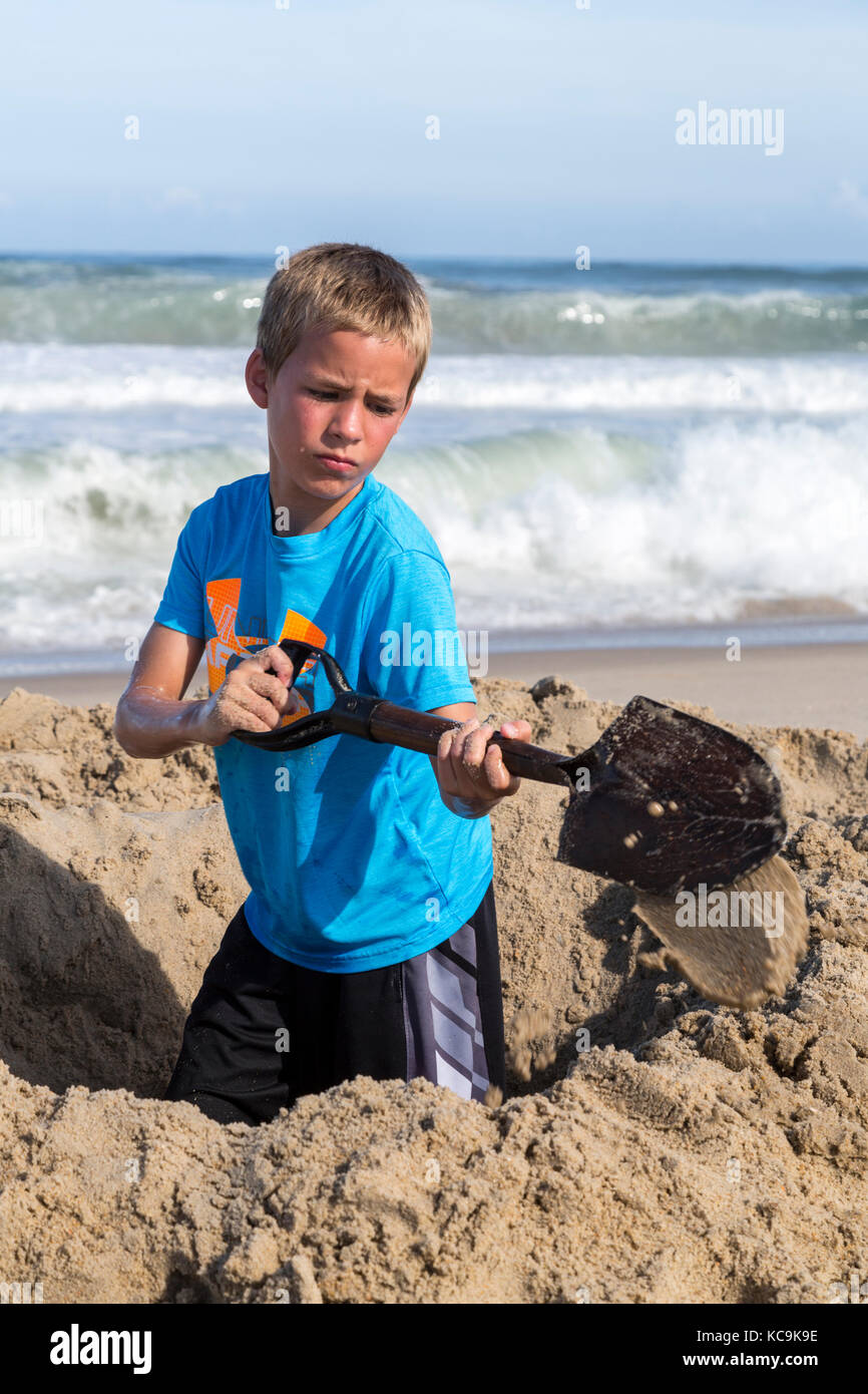 Avon, Outer Banks, Caroline du Nord, USA. Jeune garçon de creuser un trou dans le sable. Banque D'Images