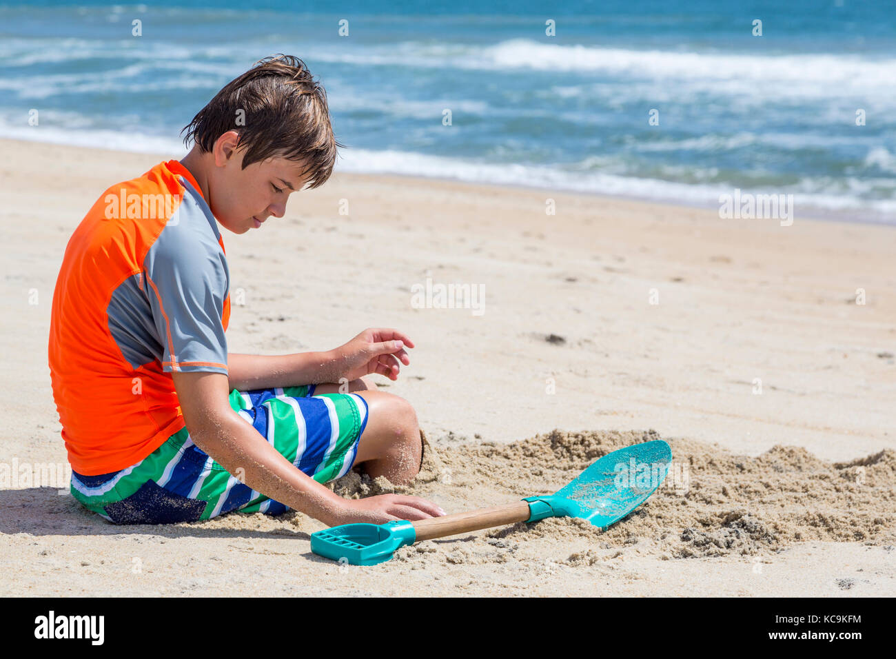 Avon, Outer Banks, Caroline du Nord, USA. Jeune garçon d'enfouir ses pieds dans le sable. Banque D'Images