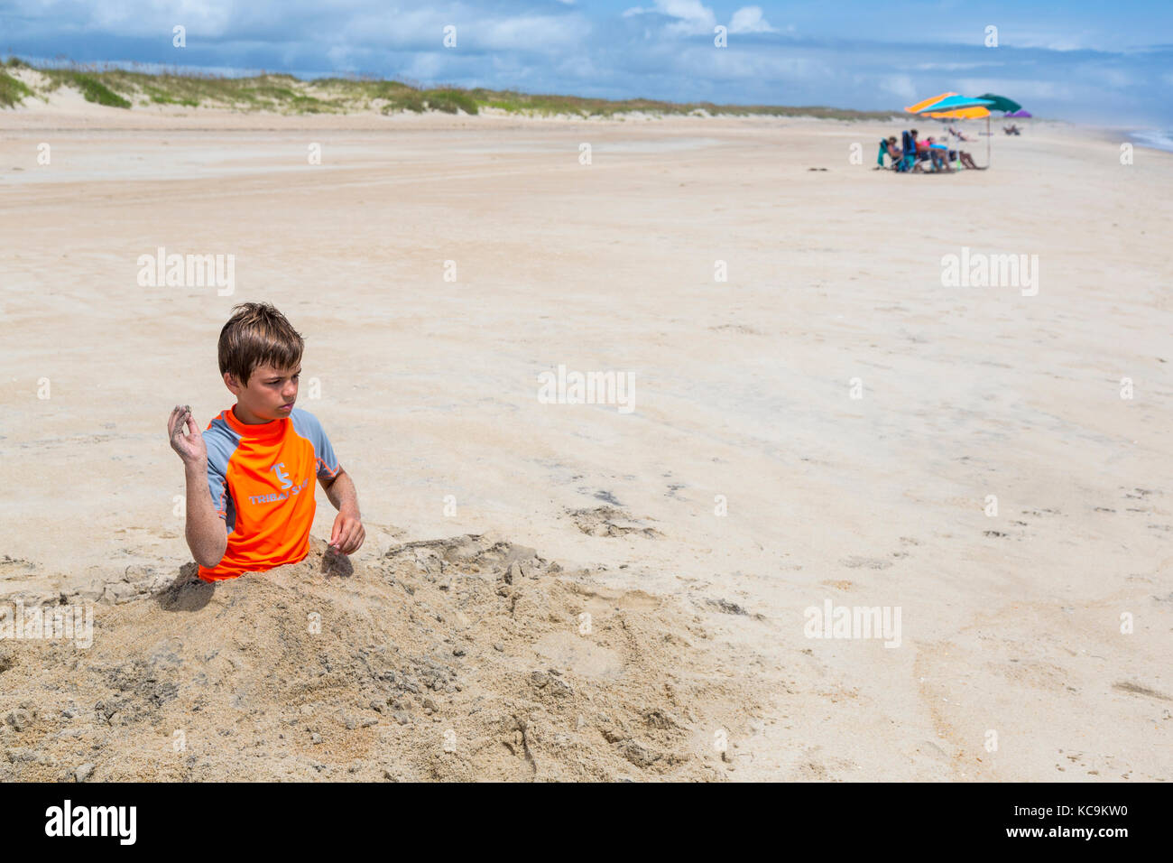 Avon, Outer Banks, Caroline du Nord, USA. Jeune garçon enterré dans le sable. Banque D'Images