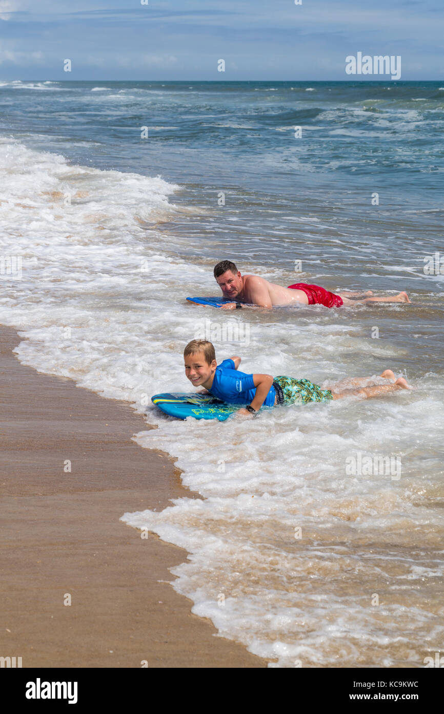 Avon, Outer Banks, Caroline du Nord, USA. Père et Fils l'atterrissage sur la plage avec leurs planches de surf. Banque D'Images