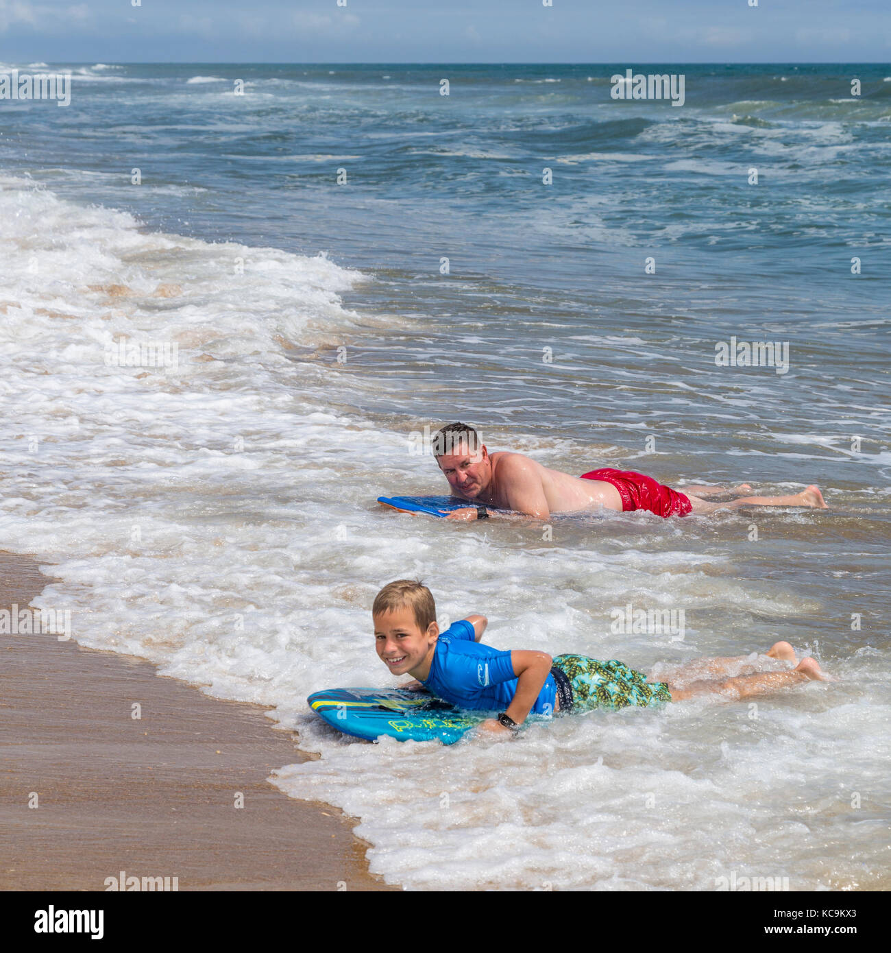 Avon, Outer Banks, Caroline du Nord, USA. Père et Fils l'atterrissage sur la plage avec leurs planches de surf. Banque D'Images