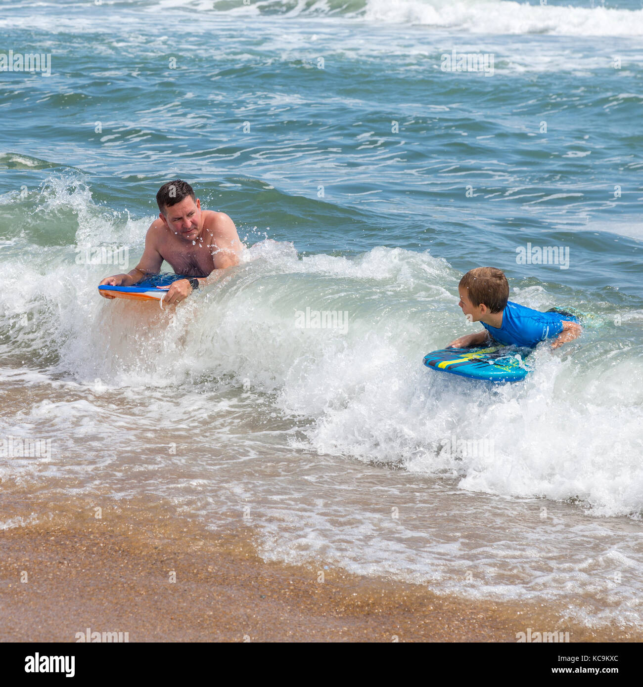 Avon, Outer Banks, Caroline du Nord, USA. Père et Fils l'atterrissage sur la plage avec leurs planches de surf. Banque D'Images