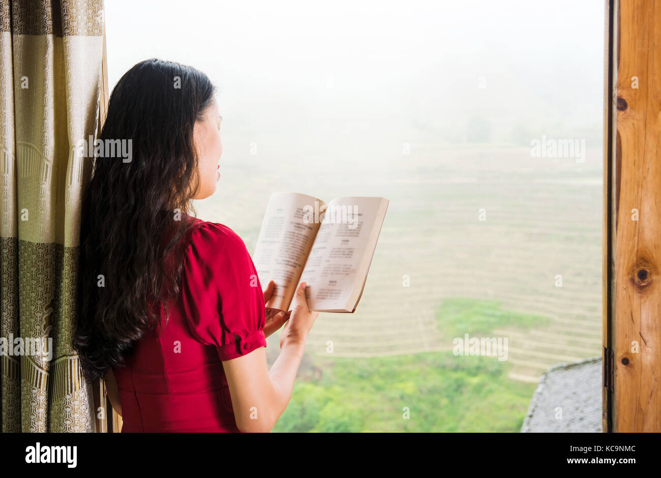 Jeune fille lisant un livre par la fenêtre avec une belle vue Banque D'Images