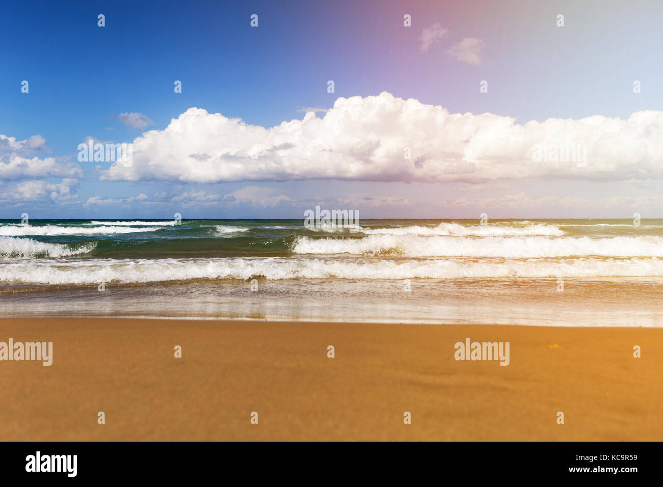 Journée ensoleillée sur la plage avec de grosses vagues et nuages blancs Banque D'Images