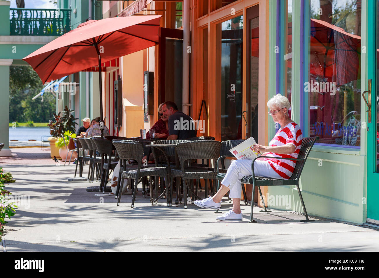 Femme lisant un journal assis à l'extérieur d'une boutique et bar, Market Street, Celebration, Orlando, Floride, l'Amérique Banque D'Images