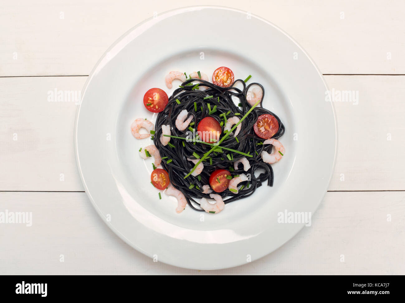 L'encre de seiche aux crevettes pâtes noires, la ciboulette et les tomates sur un fond blanc Banque D'Images