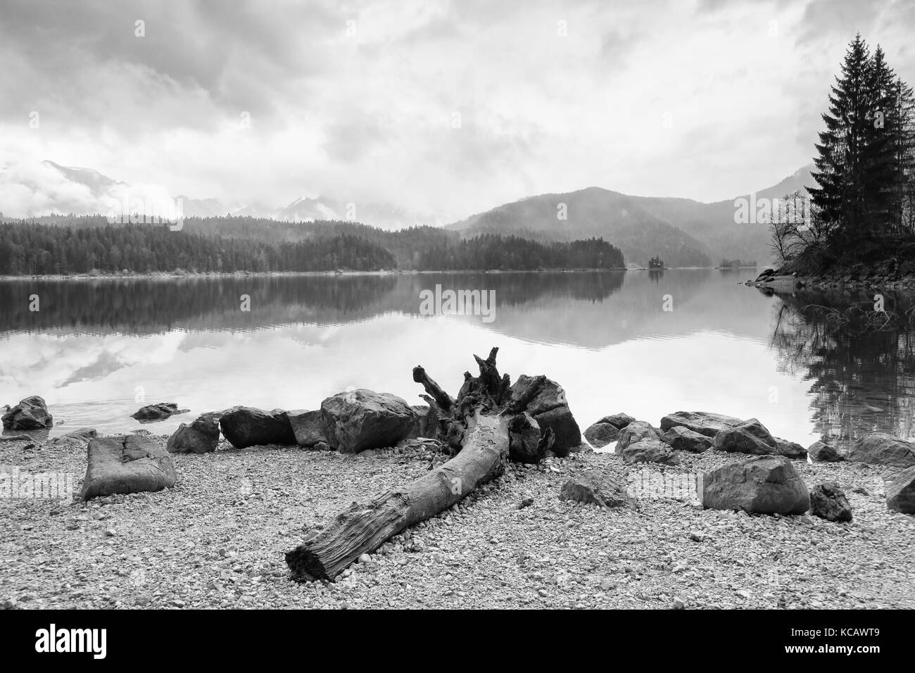 Lac de montagne avant le coucher du soleil. Le sable humide Beach avec un arbre tombé dans l'eau. ciel nuageux orageux bove montagnes bleues à l'horizon.. Mauvaise condition d'éclairage Banque D'Images