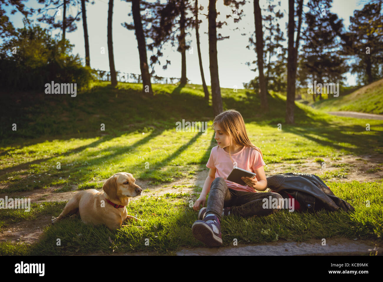 Fille assise dans le parc avec un chien et à l'aide de tablet Banque D'Images