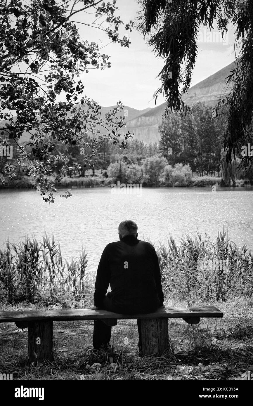 Homme assis sur un banc avec vue sur le lac. Image en noir et blanc. Banque D'Images
