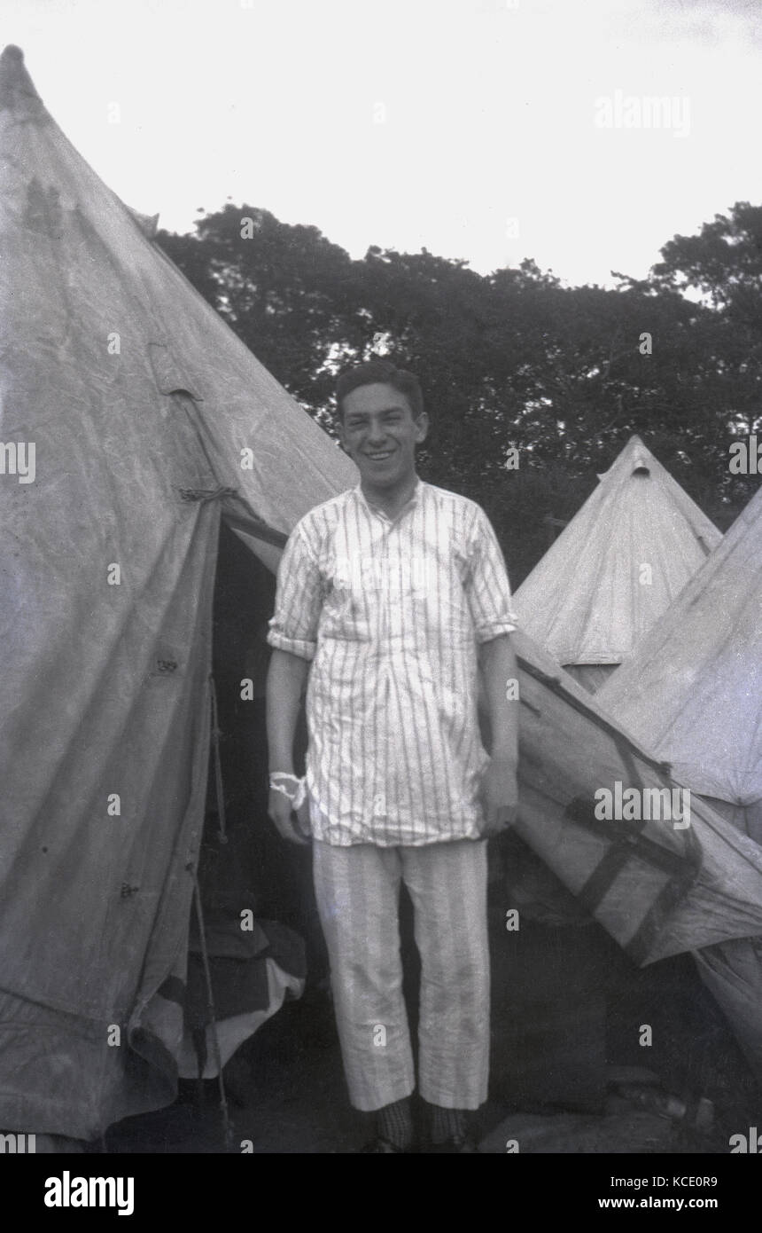 @1930, historique, l'image montre un homme debout à l'attention portant des pyjamas rayés, à l'extérieur de l'ouverture de sa tente en toile de coton traditionnel, montrant son lit de camp, England, UK. Banque D'Images