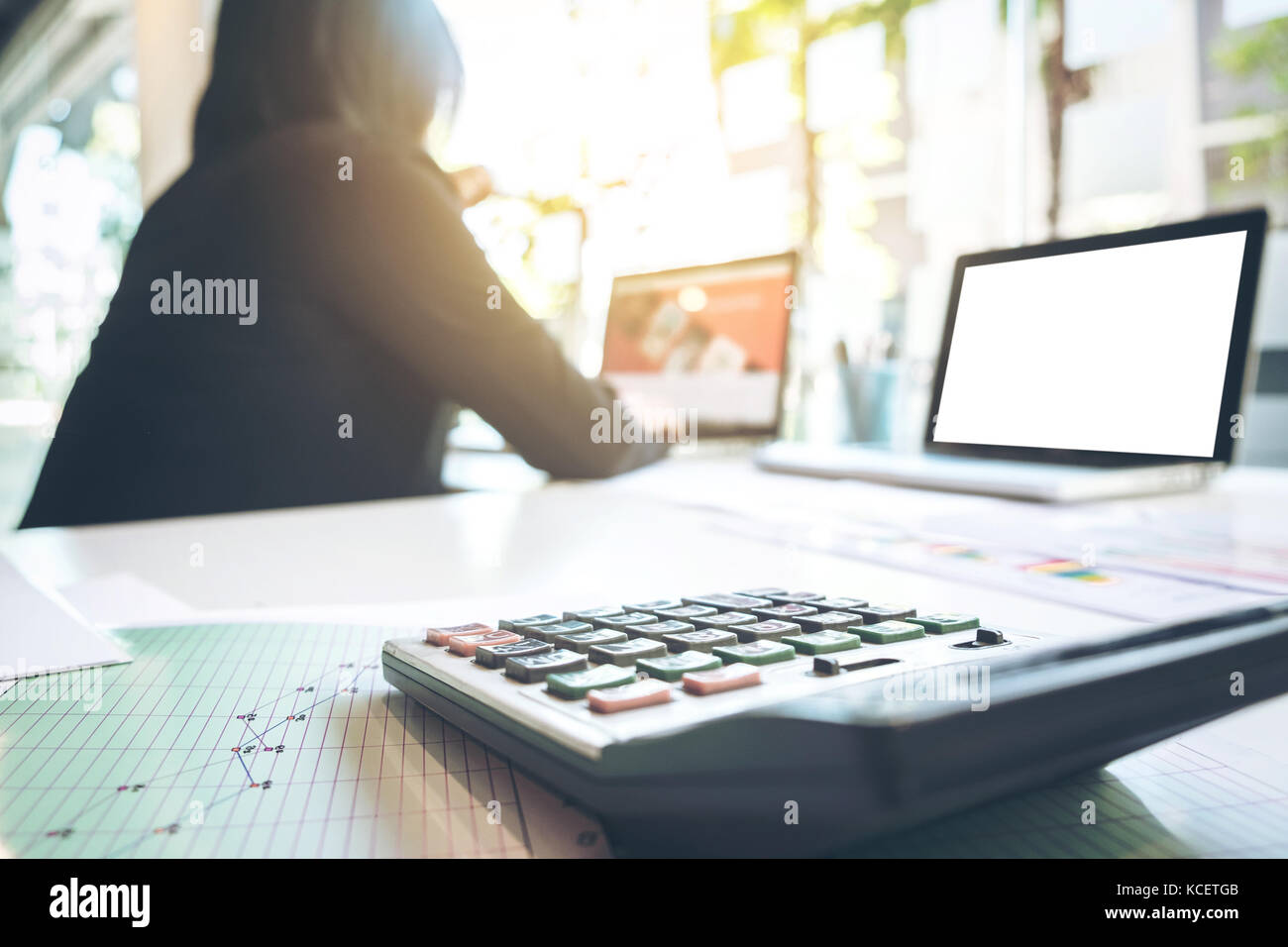 Businesswoman using laptop et calculatrice de bureau à bureau et de nombreuses données document graphique dans la lumière du matin, concept d'entreprise. Banque D'Images