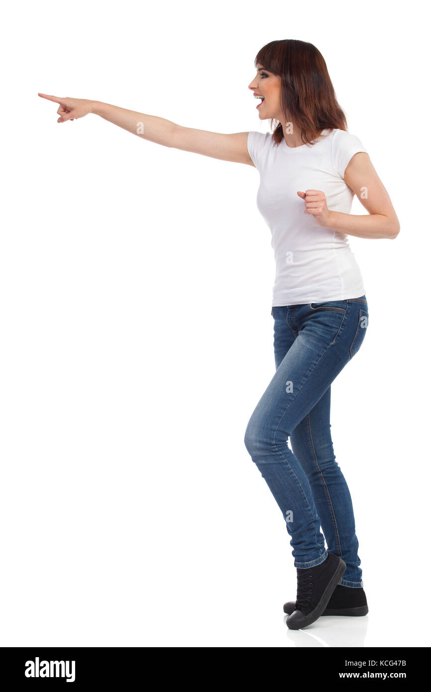 Happy young woman en jeans, T-shirt blanc et baskets bras tendus, est orienté et crier. Vue de côté. toute la longueur isolée studio shot Banque D'Images