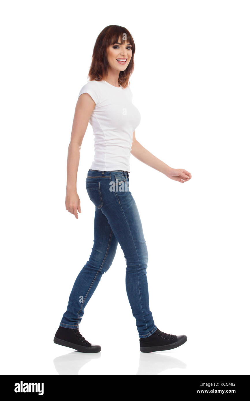 Jeune femme en jeans et t-shirt blanc est la marche, looking at camera and smiling. full length portrait isolé sur blanc. Banque D'Images