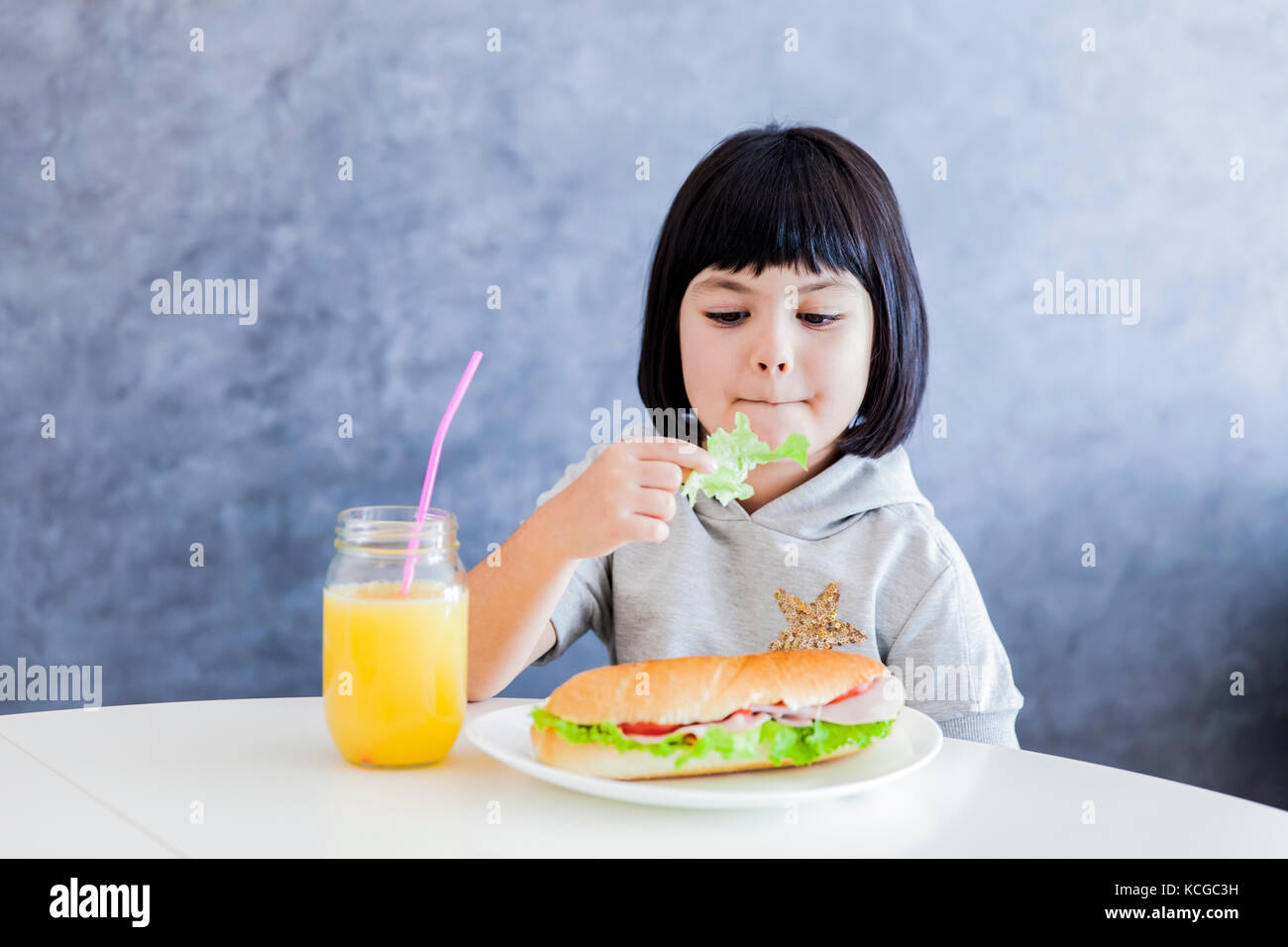 Les cheveux noirs de seiches petite fille de prendre le petit déjeuner et manger la laitue à Accueil Banque D'Images