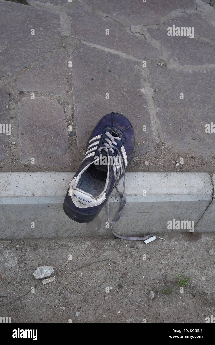 Une vieille chaussure formateur sur la chaussée laissé à l'abandon par son propriétaire Banque D'Images