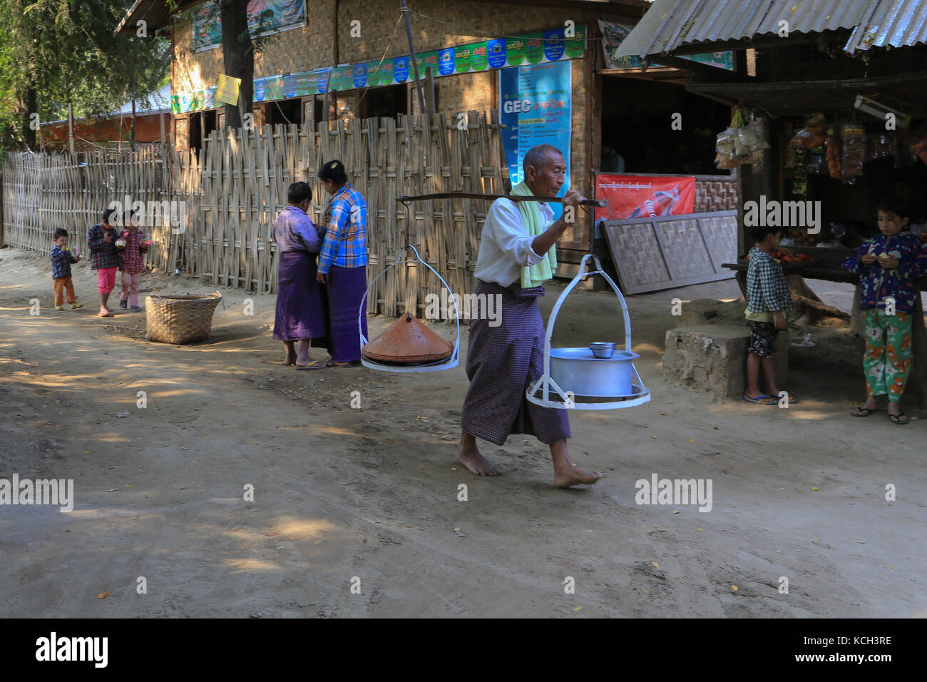 Un homme à Yandabo Village sur le Fleuve Irrawaddy en Birmanie (Myanmar) réalise des pots de nourriture alors que les enfants et les femmes sont à proximité d'un magasin. Banque D'Images