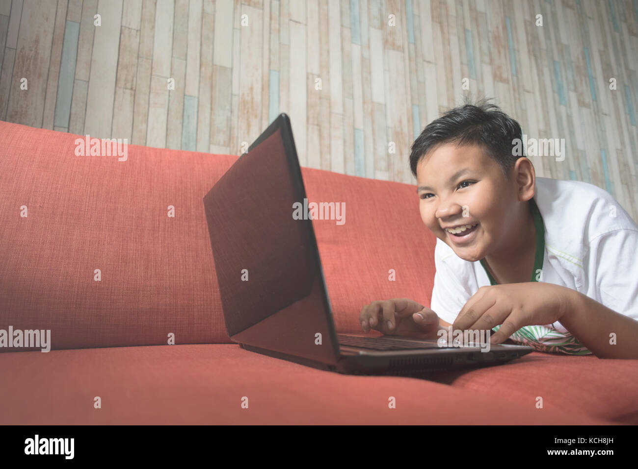 jeune garçon asiatique utilisant un ordinateur portable sur un canapé à la maison. garçon se relaxant sur le canapé à la maison. le garçon sourit. Technologie / concept INFORMATIQUE. Conc. Apprentissage informatique Banque D'Images