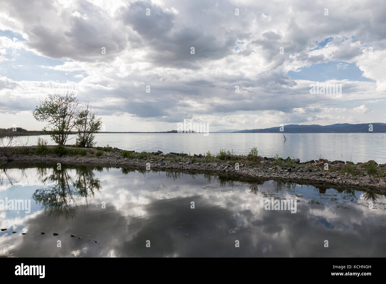 Un quai dans un lac, avec un beau ciel bleu profond avec des nuages blancs réfléchissant sur l'eau, avec quelques arbres Banque D'Images