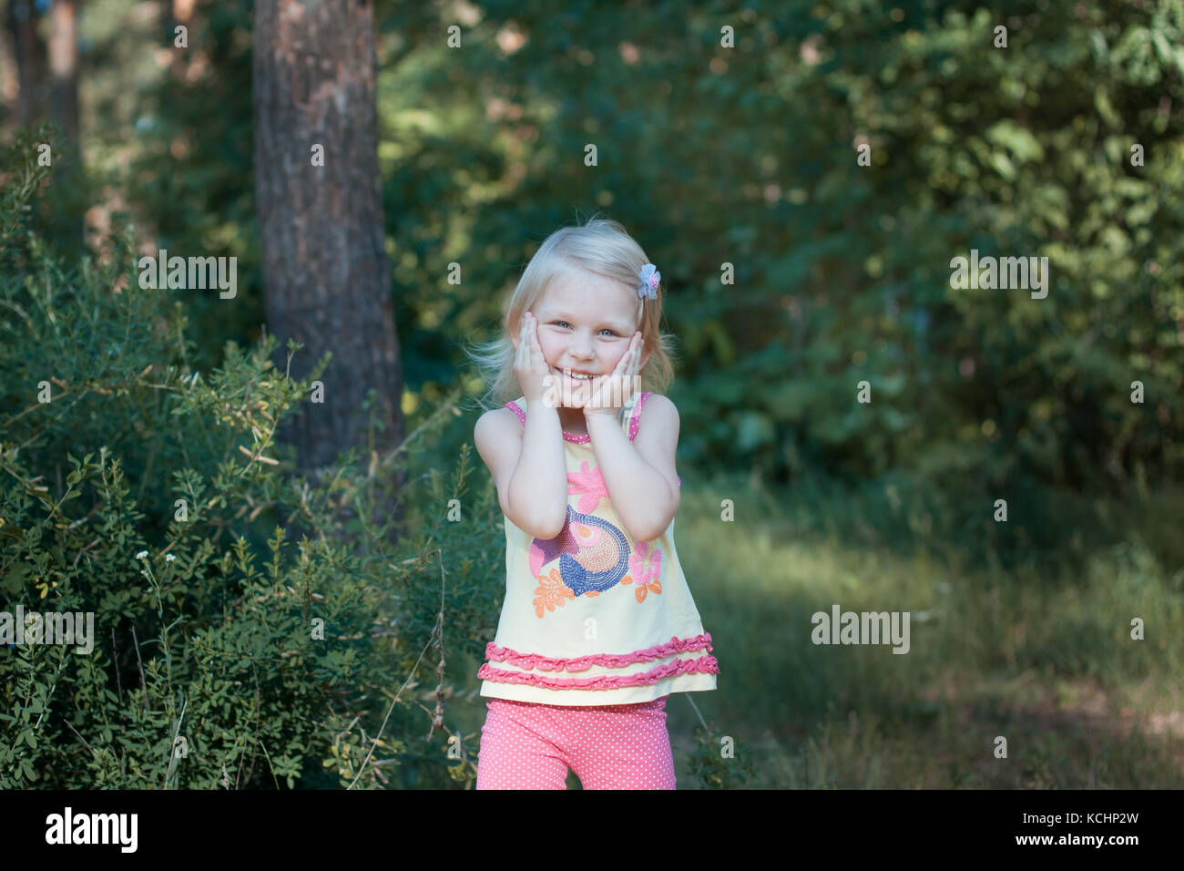 Peu de belle fille blonde debout dans les bois. elle rit elle les mains jointes Banque D'Images